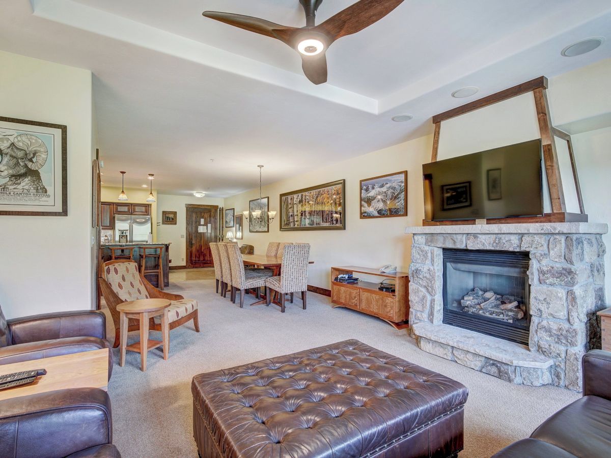 Bright living room with a stone fireplace, wall TV, dining table, framed art, ceiling fans, and plush seating.