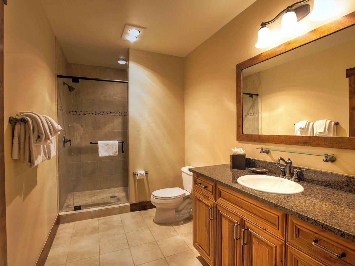 A well-lit bathroom with a glass shower, towel rack, toilet, granite vanity with sink, and a wall mirror.