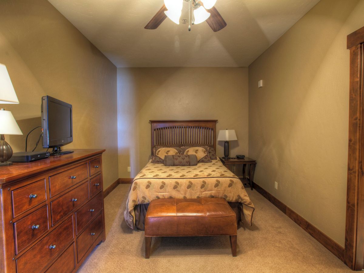 A cozy bedroom with a bed, dresser, TV, lamps, and a ceiling fan with lights.