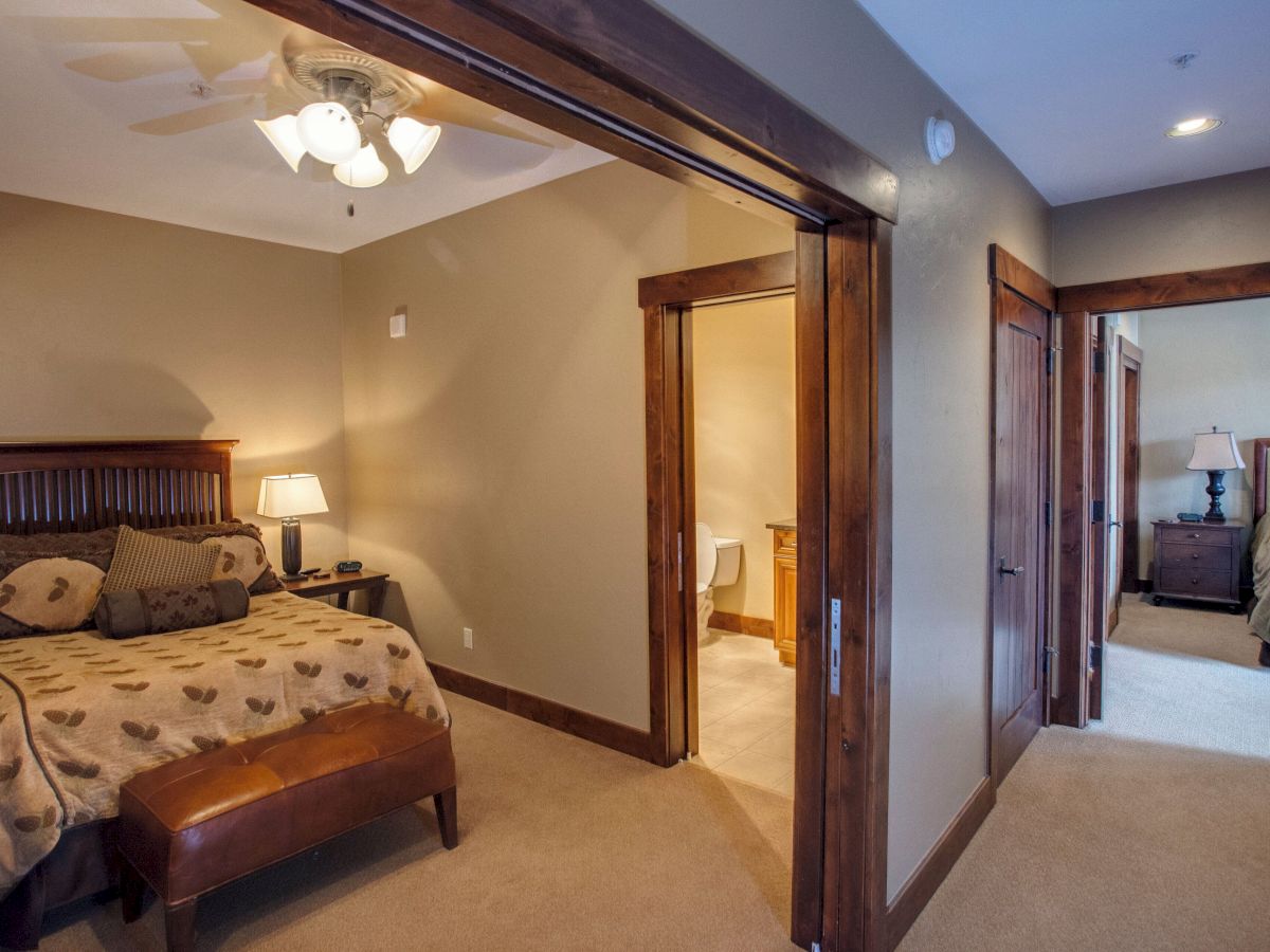 A cozy bedroom with a bed, ceiling fan/light, lamp, and open wooden door leading to a hallway.