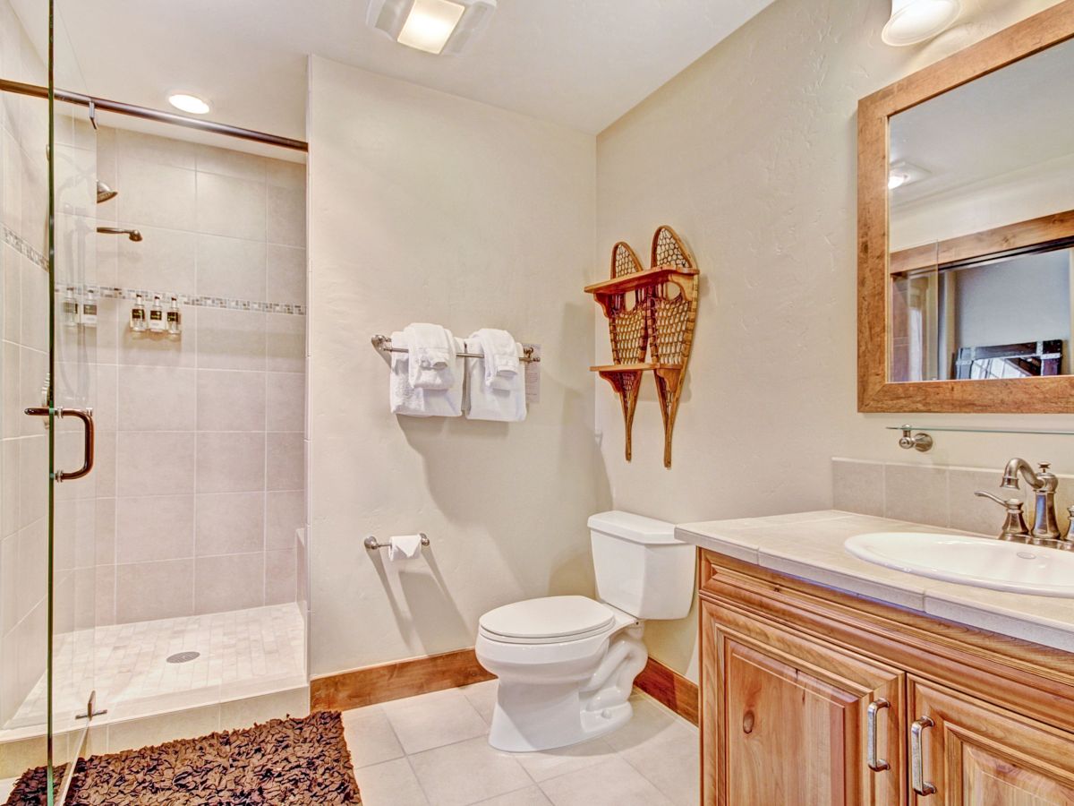 A modern bathroom with a tiled walk-in shower, toilet, vanity with sink, mirror, towels, and warm ceiling lights.