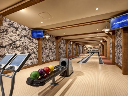 An indoor bowling alley with wooden lanes, bowling balls on a ball return, and TVs showing Brunswick branding.