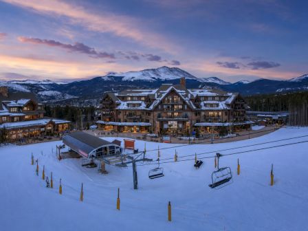 Snowy ski resort with wooden chalets and a chairlift on a mountain slope at sunset.