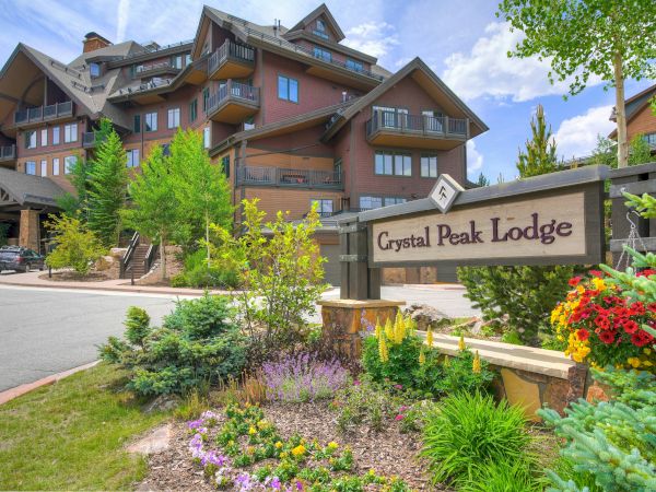 A landscaped resort entrance with a sign reading Crystal Peak Lodge and a multi-story brick building under a blue sky.