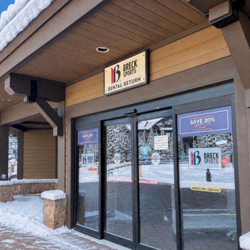 A snowy storefront for Breck Sports, with a &ldquo;Rental Return&rdquo; sign and &ldquo;Save 20%&rdquo; promo on the glass doors, outside in winter.