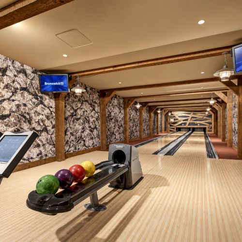 A wooden bowling alley with polished lanes, bowling balls on the approach, and Brunswick screens lining the walls.