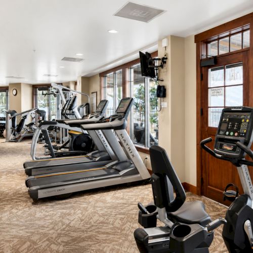 A bright gym with multiple treadmills, exercise equipment, and windows along one wall.