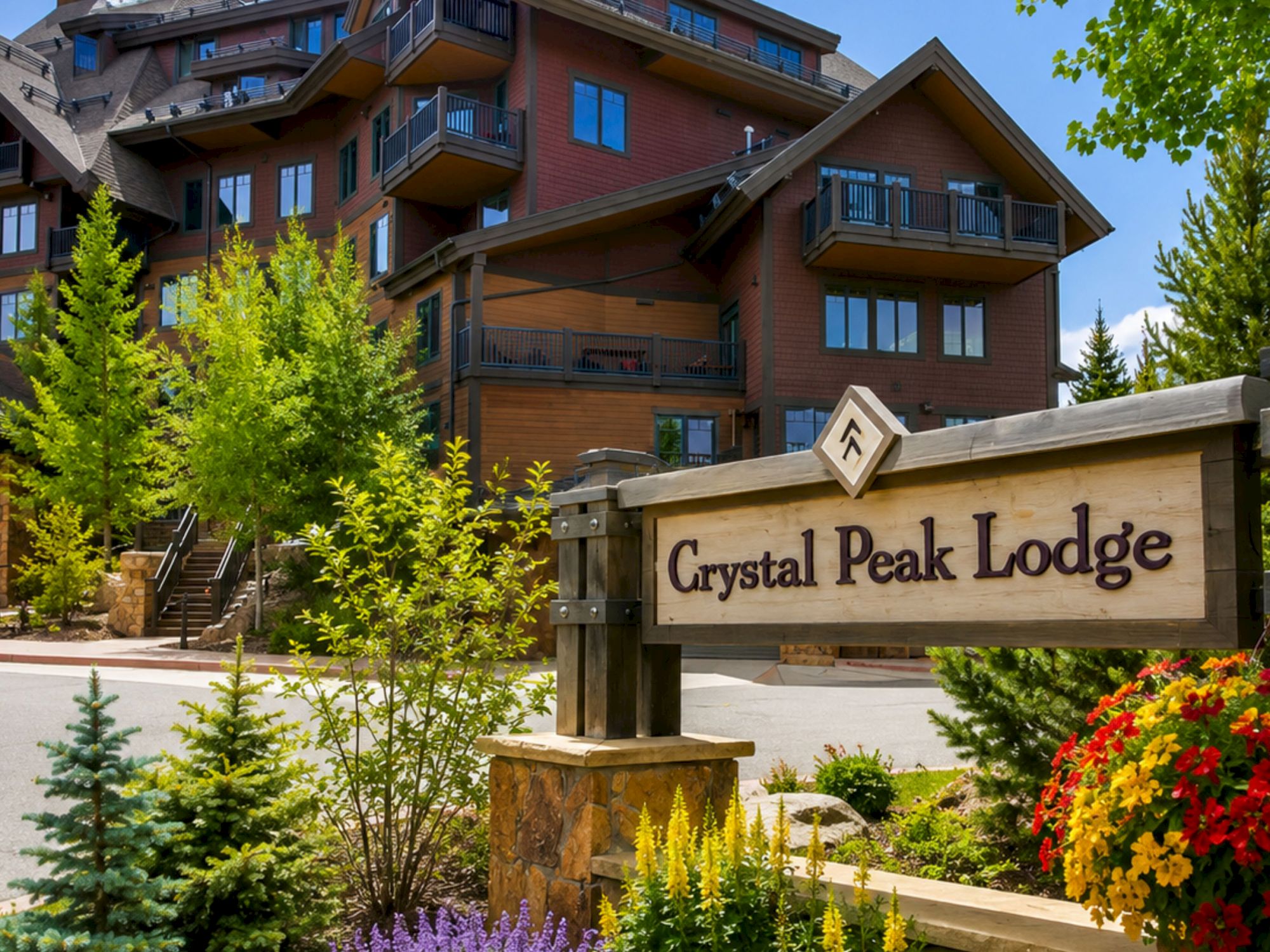 Exterior of a brick apartment building with balconies and the sign &ldquo;Crystal Peak Lodge,&rdquo; surrounded by bright landscaping.